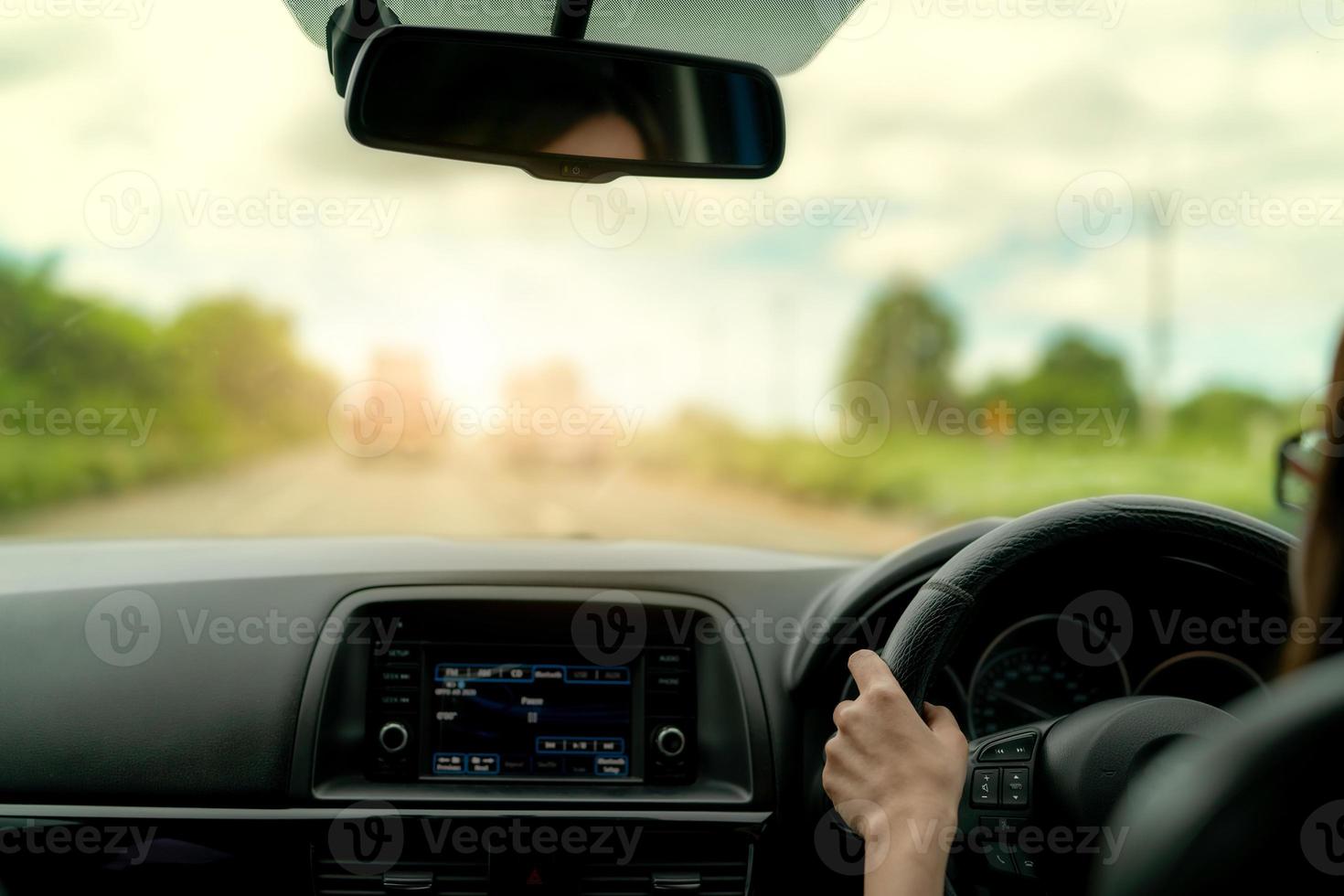 Back view of a woman driving car for summer road trip travel. Car driving with safety on asphalt road. Driver hand holding steering wheel for control car. Inside view of car. Dashboard and windshield. photo