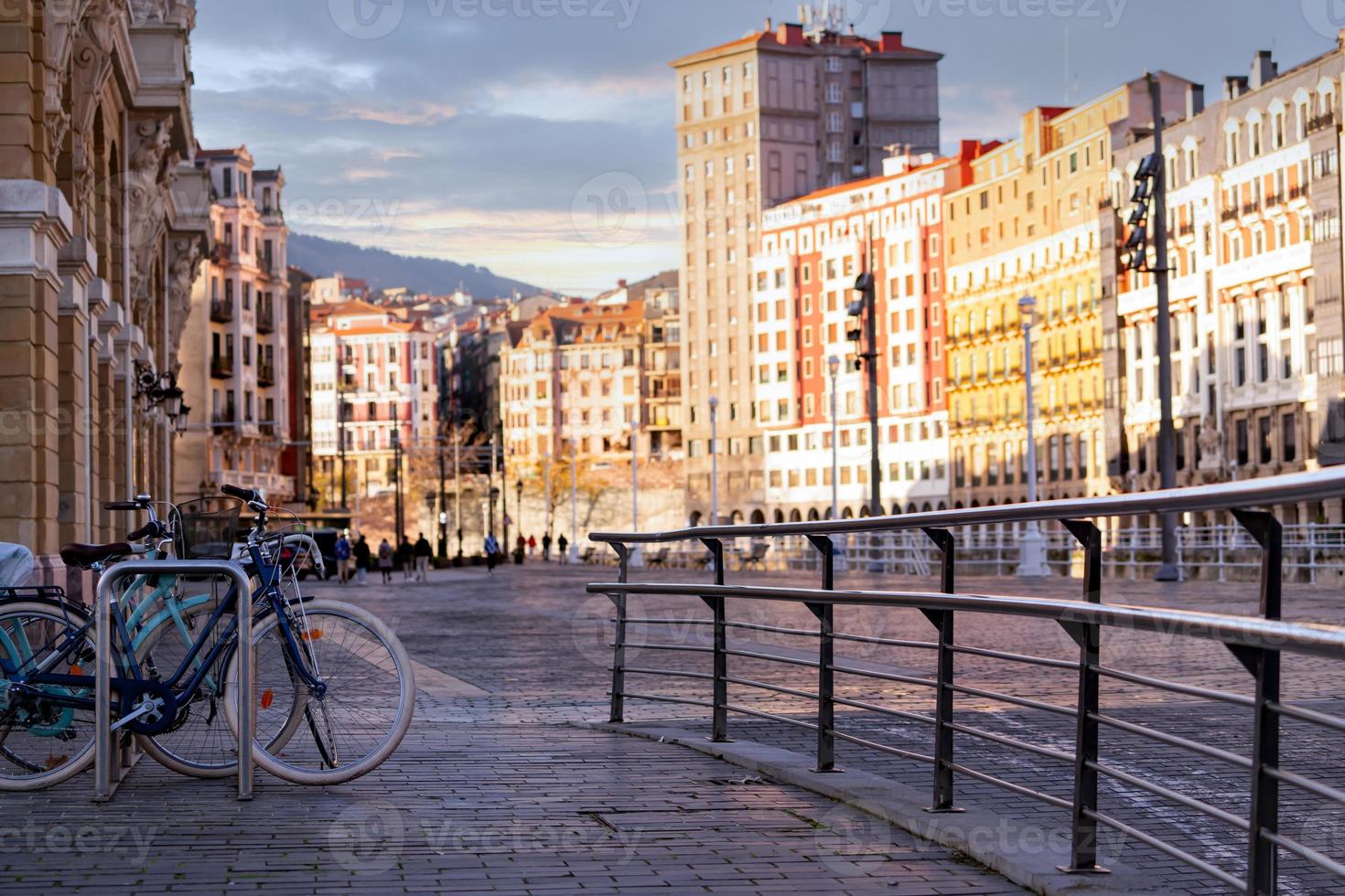 bicicleta en la estación de bicicletas para viajes o transporte en la ciudad de europa. viajes sostenibles. sistema de bicicletas compartidas. bicicleta estacionada en la estación de gente borrosa y edificio antiguo en españa. transporte ecológico. foto