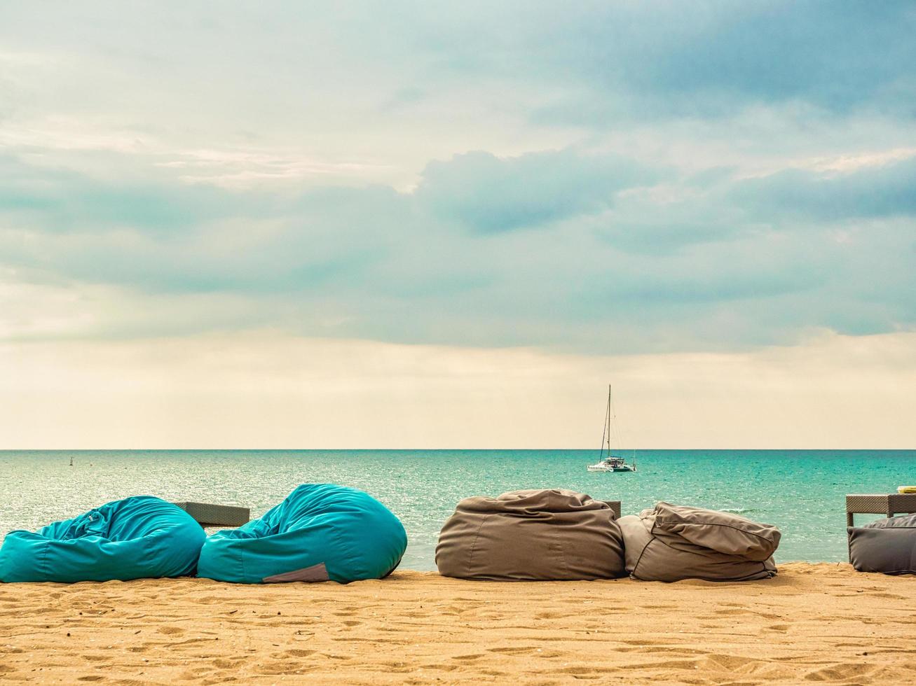 Bean bags on beach with sailing yacht in the sea and blue sky, beautiful view. photo