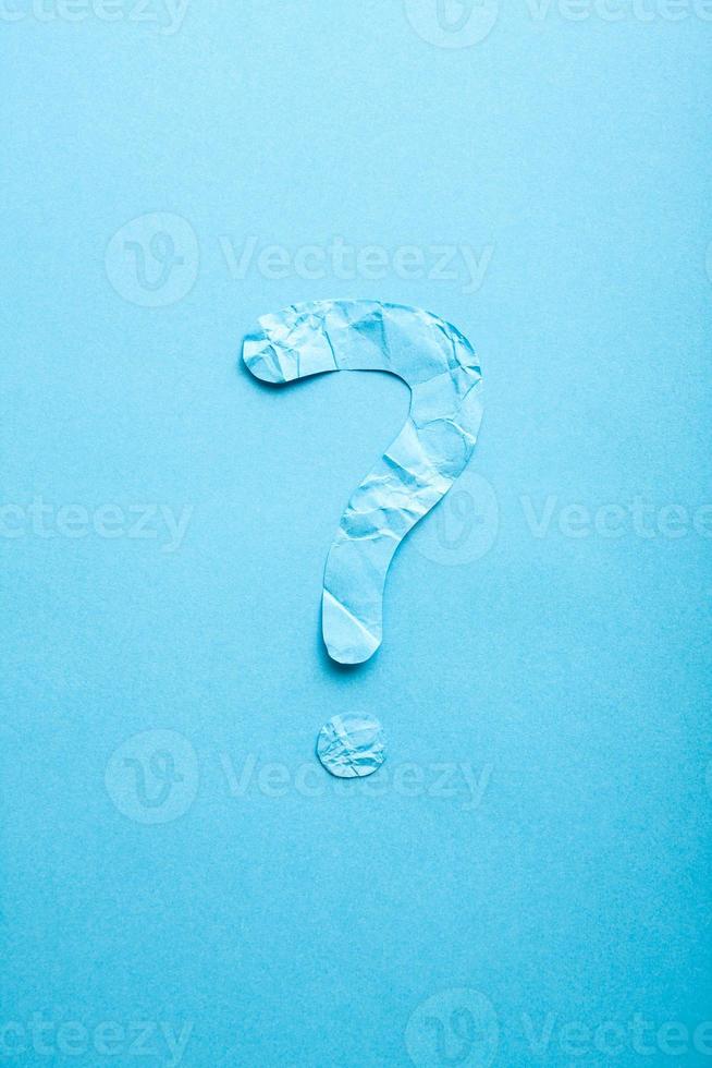 Crumpled paper question mark on blue paper background. photo