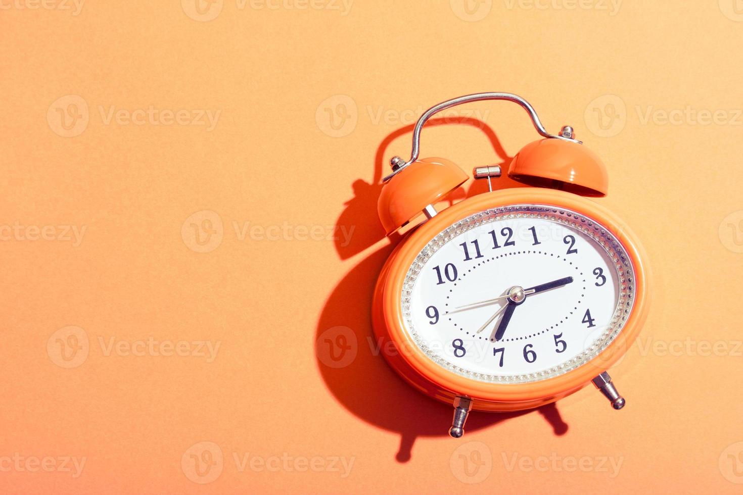 Orange retro style alarm clock on orange background under the bright sunlight, photo