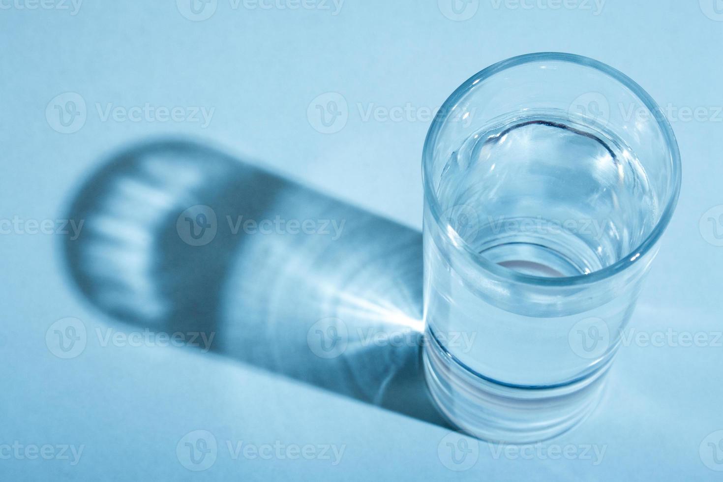 Glass of clean water with shadow in blue monochrome. photo