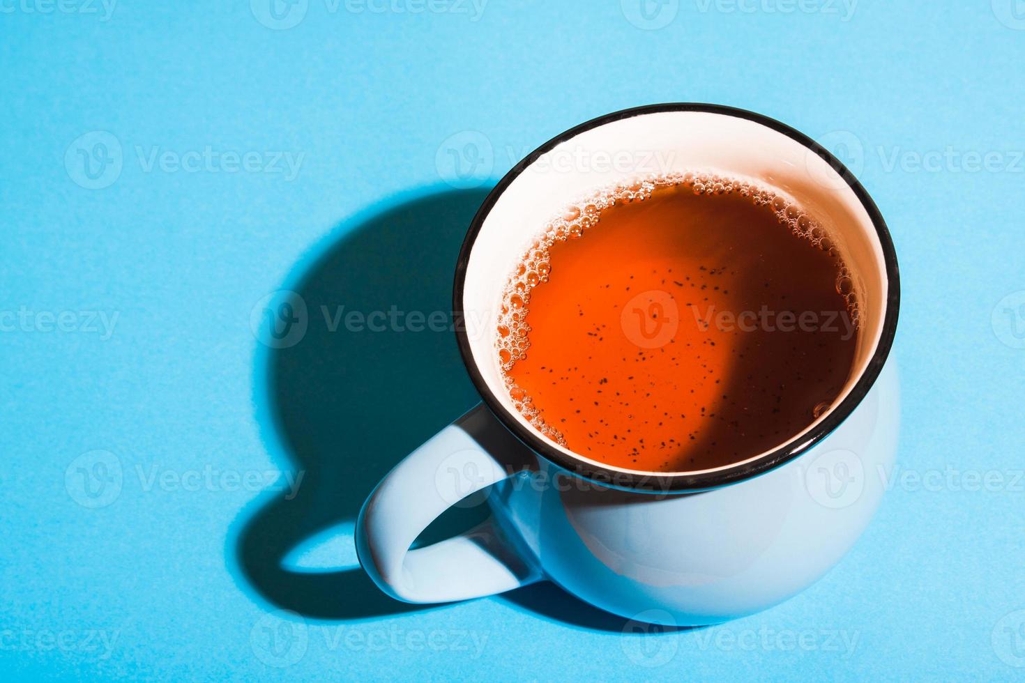 una taza de té negro sobre fondo azul bajo la brillante luz del sol. foto