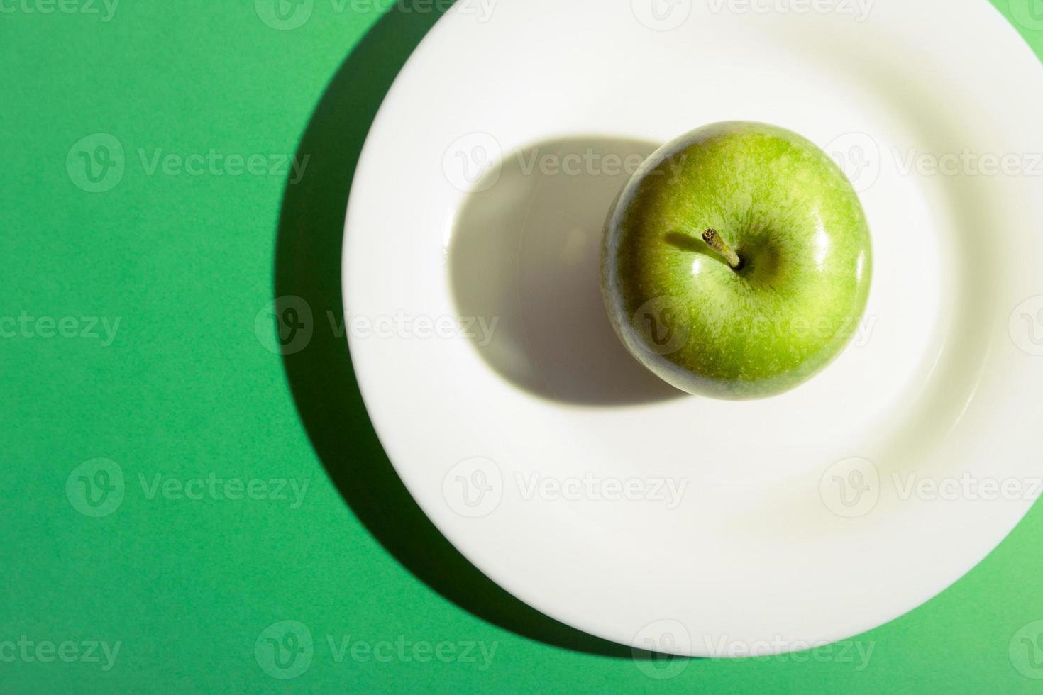 Green apple on a white plate. Granny Smith green apple with dark shadow. photo