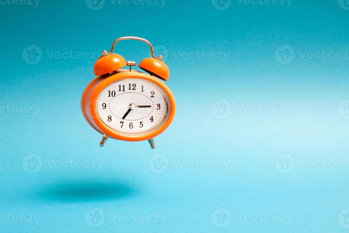 reloj despertador volador de estilo vintage naranja. despertador volador sobre fondo azul. foto