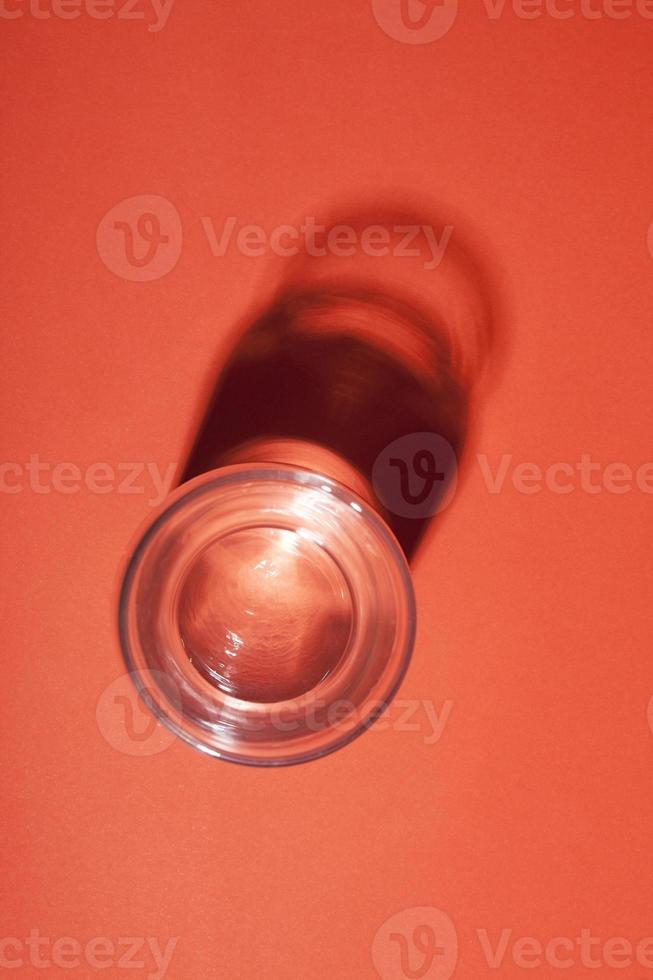 Glass of water with abstract dark shadow on red background. photo