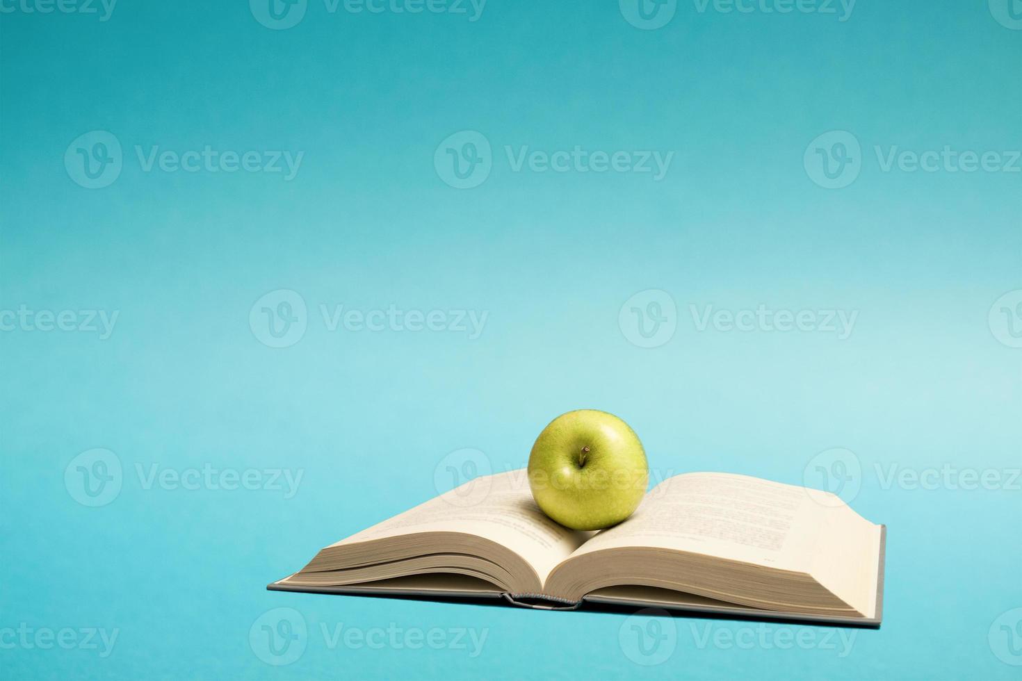 Education knowledge concept still life image with free space for text. Green apple on an open book on blue background. photo