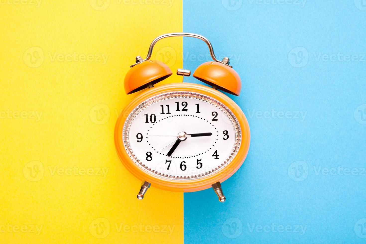 Orange vintage style alarm clock on blue and yellow background. photo