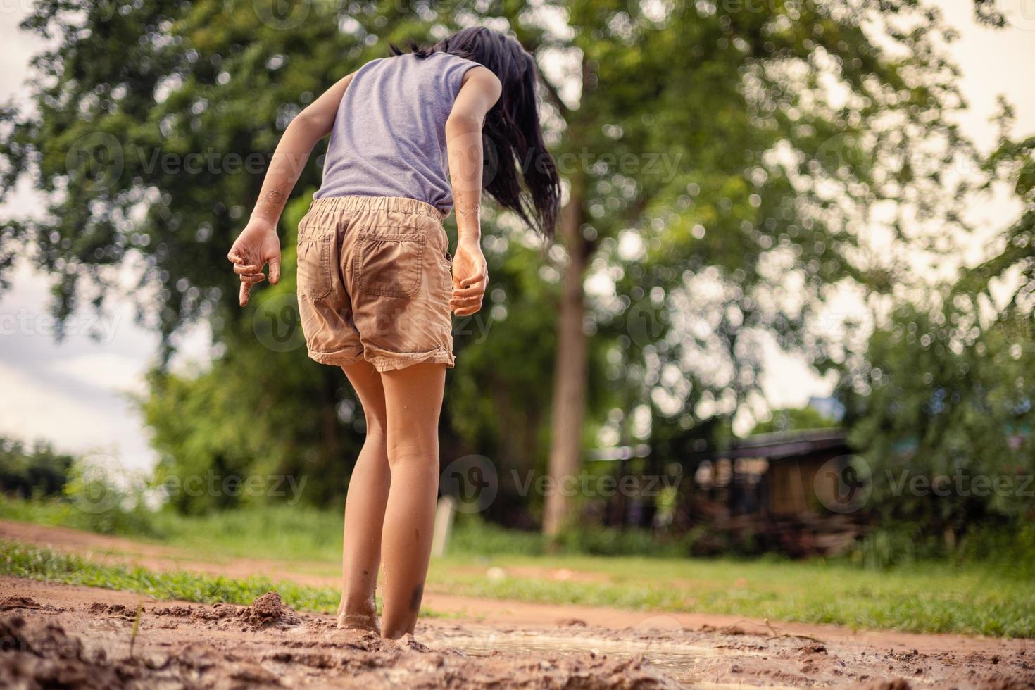 A little Asian girl plays with soil in nature at his house during the day. photo