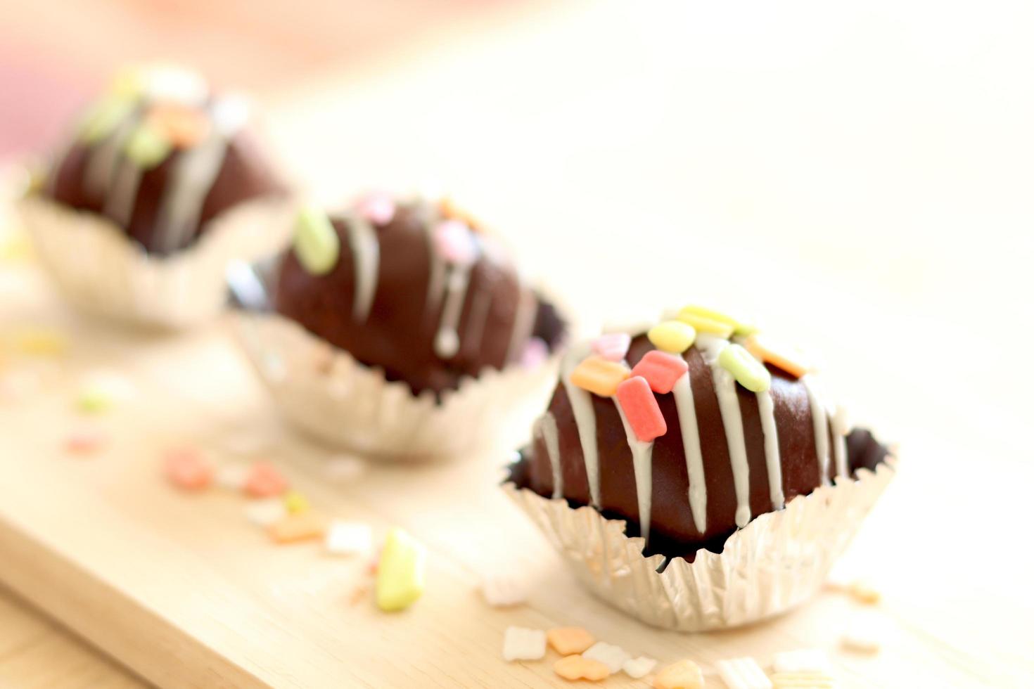 deliciosa bola de pastel de chocolate de postre dulce con cobertura colorida en una taza de papel de aluminio sobre tabla de madera. foto