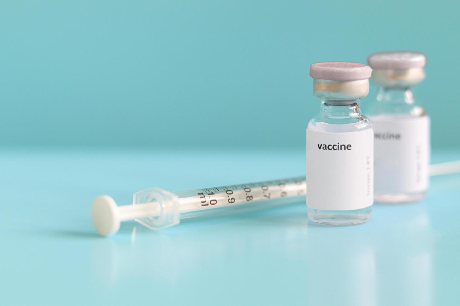 Glass vials containing liquid medical vaccine used to shot for injection treatment with needle syringe on blue background and copy space, vaccination and immunization care for prevent virus outbreak photo