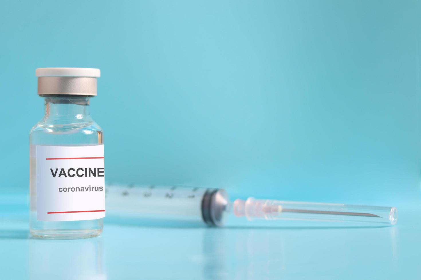 Glass vial contain liquid medical vaccine used to shot for injection treatment with blurred needle syringe on blue background and copy space, vaccination and immunization care for prevent virus photo