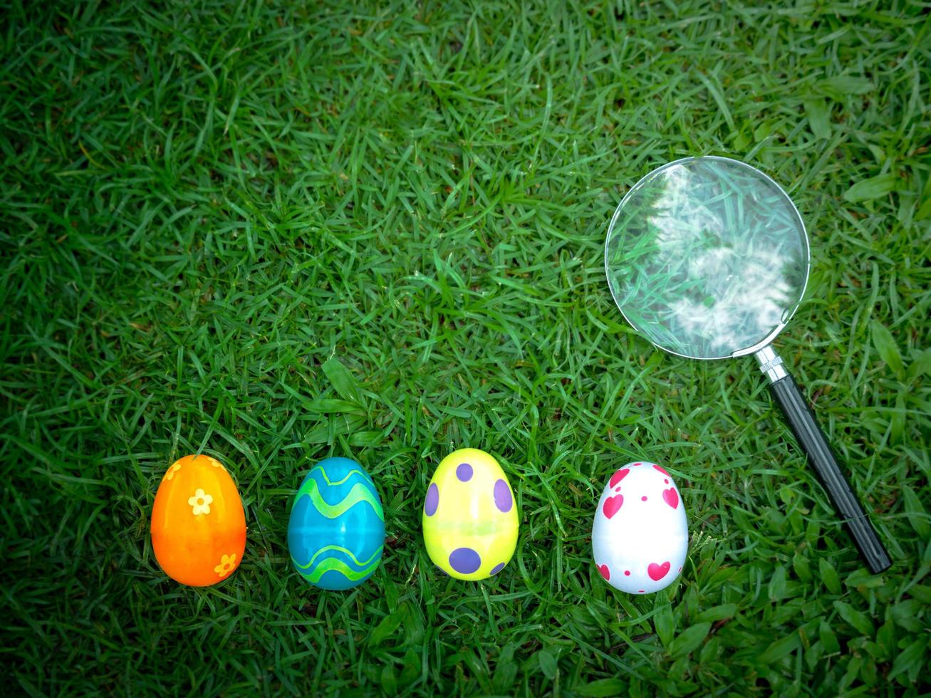 Colorful Easter eggs on green grass with magnifying glass, Easter egg hunter photo