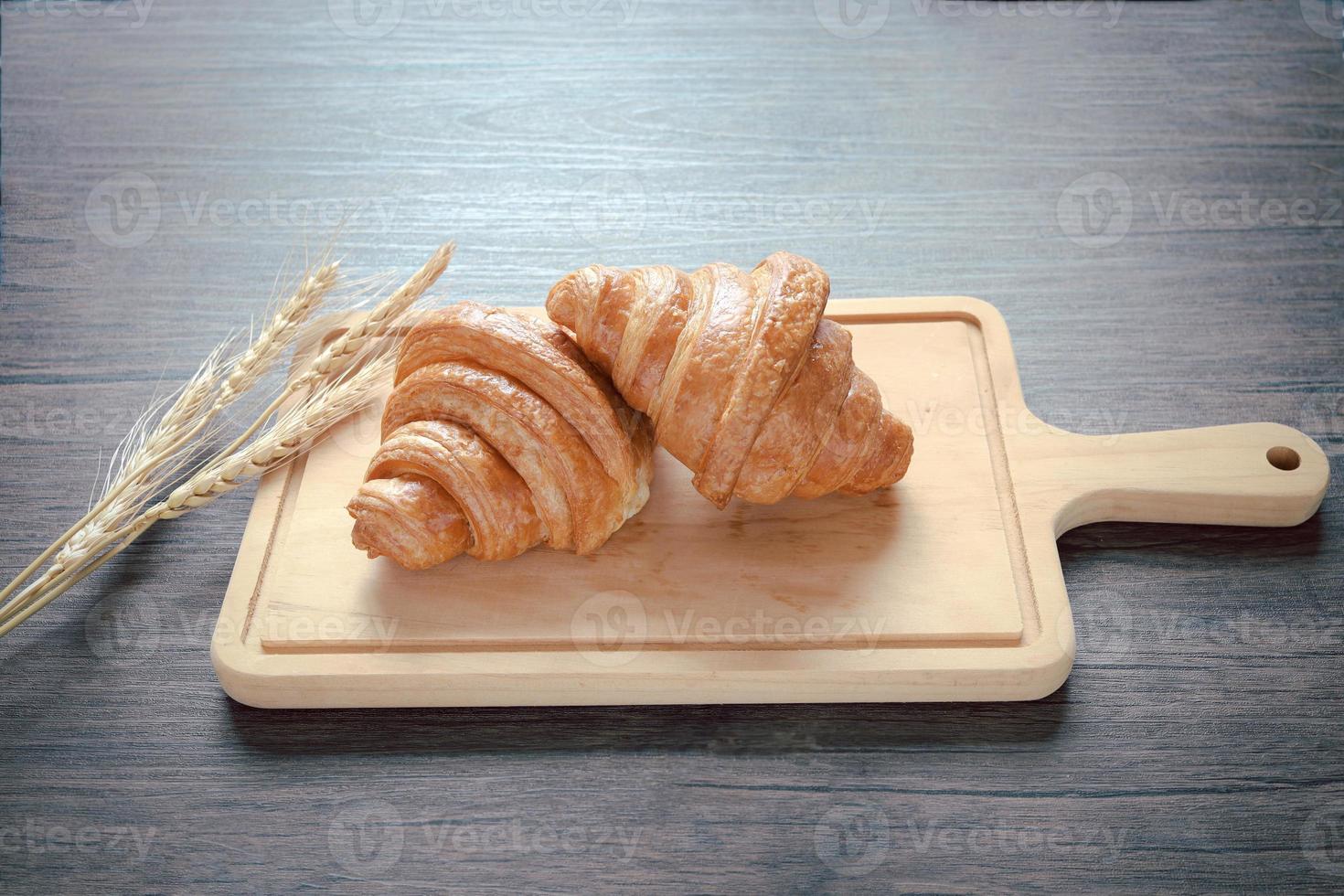 Two freshly baked delicious croissants with spikelets on wooden cutting board, food on breakfast table photo