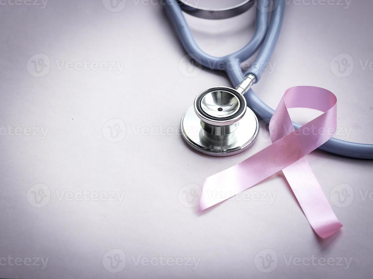 cinta rosa de concientización sobre el cáncer de mama con estetoscopio médico sobre fondo rosa, símbolo de octubre, concepto de salud y medicina foto