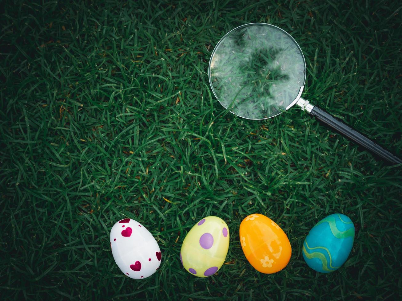 Colorful Easter eggs on green grass with magnifying glass, Easter egg hunter photo