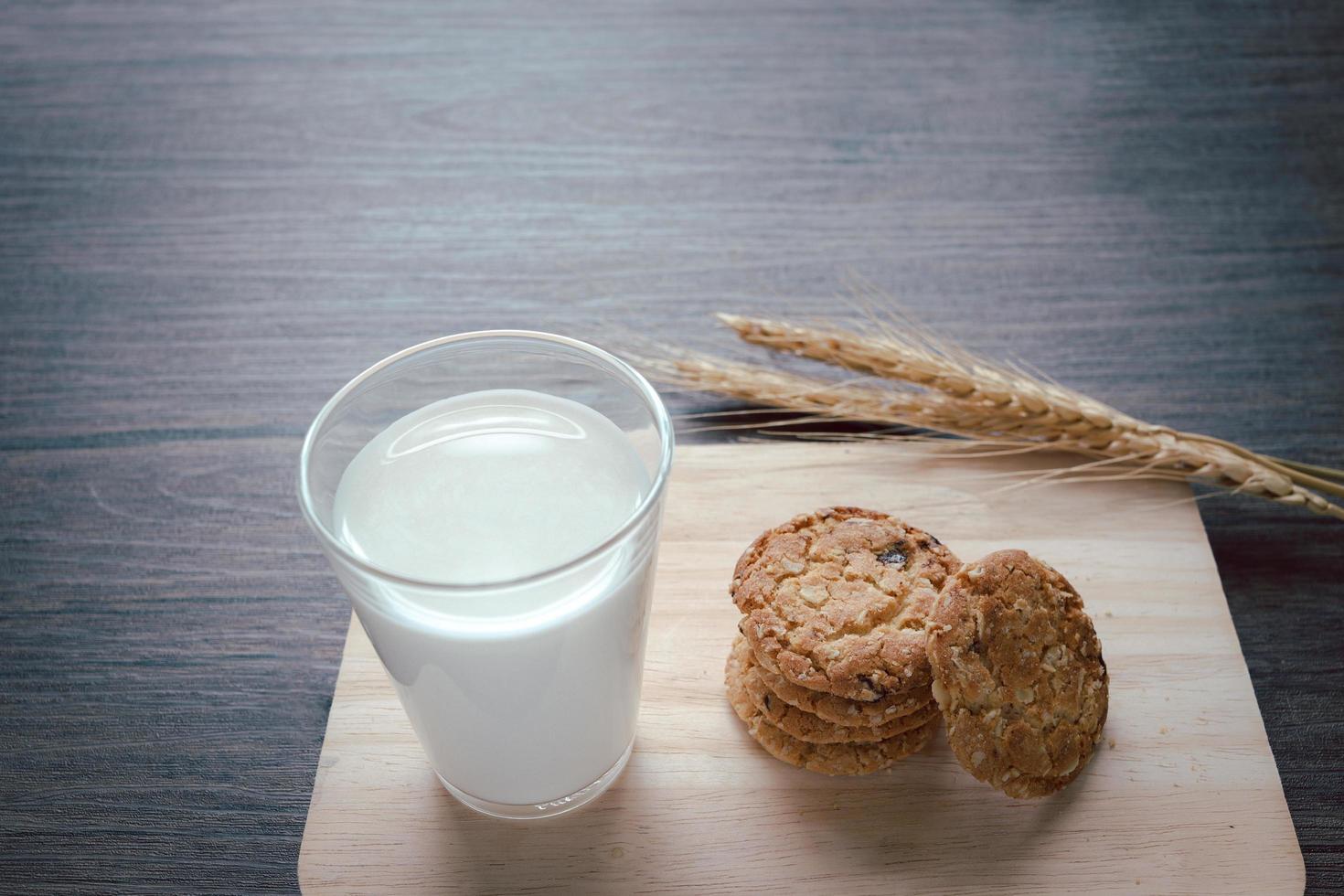 Delicious oatmeal cookies with spikelets and glass of milk on wooden cutting board on table. photo