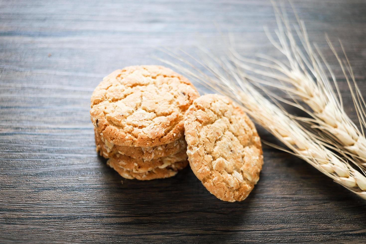 Delicious oatmeal cookies with spikelets on dark wooden table. photo