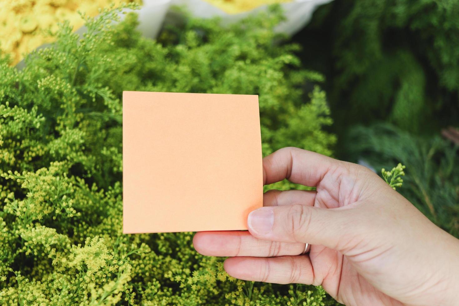 Blank note paper in hand on beautiful flower bouquet background, copy-space on card to put your message. photo