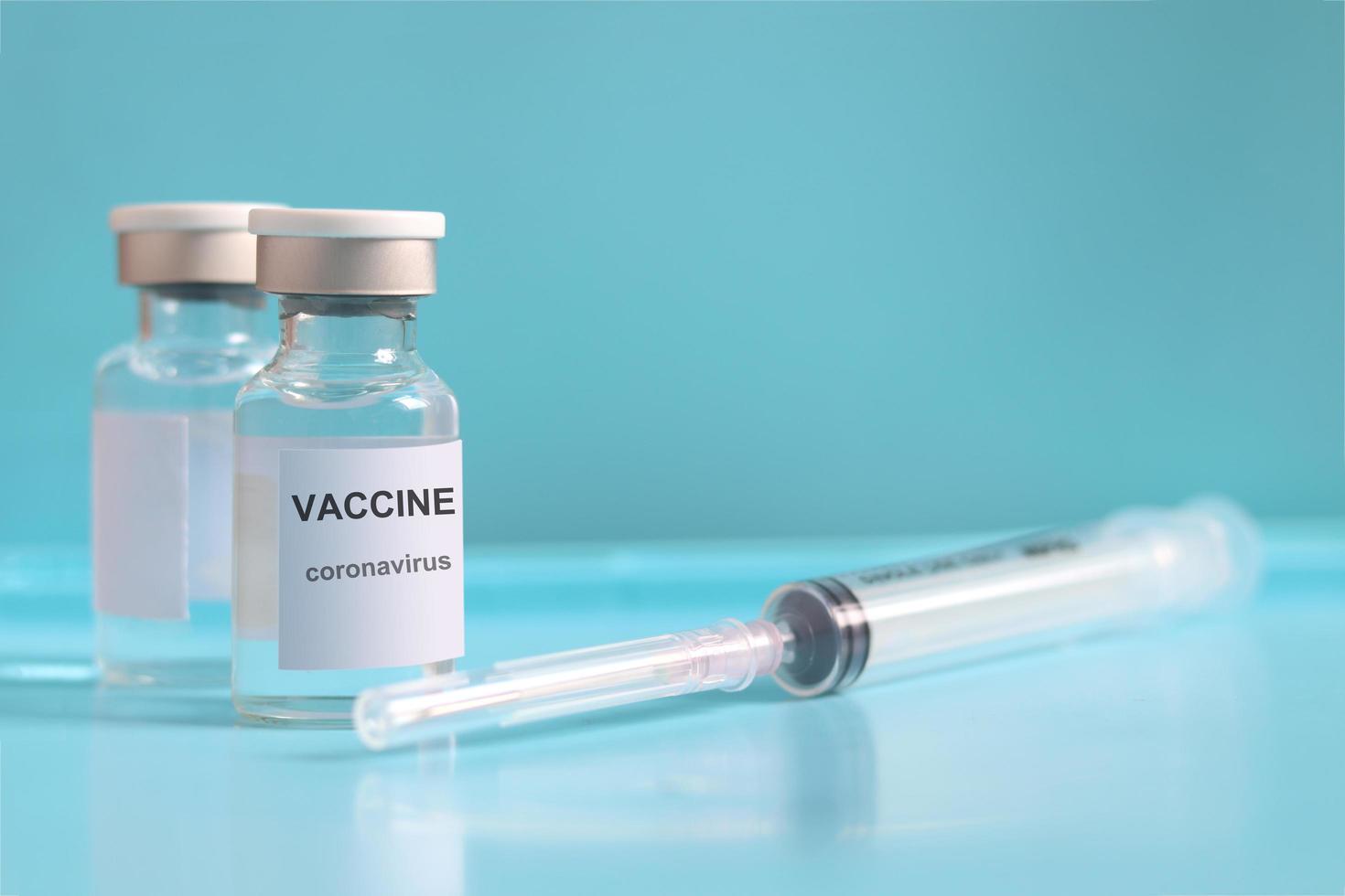 Glass vials contain liquid medical vaccine used to shot for injection treatment with blurred needle syringe on blue background and copy space, vaccination and immunization care for preventing virus photo