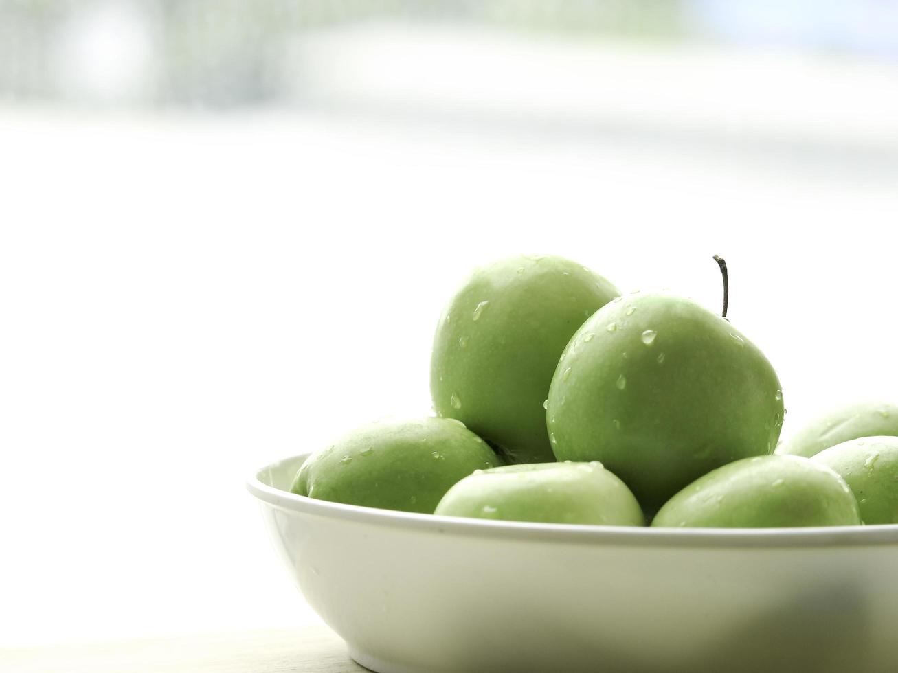 fruta cruda de manzana verde madura en un tazón blanco sobre una mesa de madera, productos frescos orgánicos saludables foto
