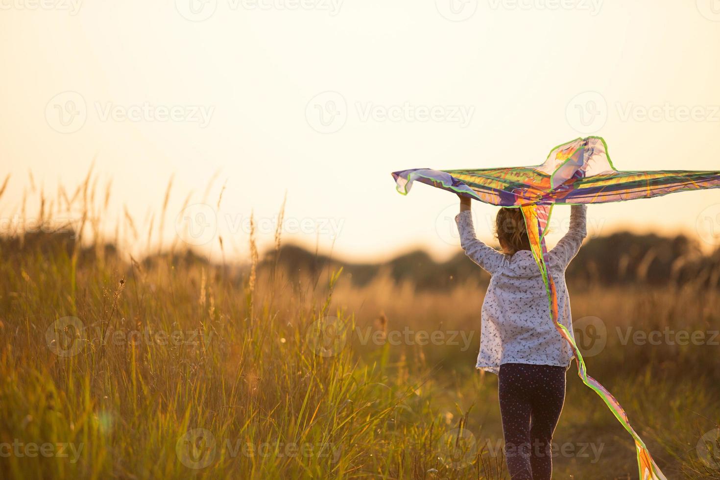 una niña corre a un campo con una cometa, aprende a lanzarla. animación al aire libre en verano, naturaleza y aire puro. infancia, libertad y despreocupación. un niño con alas es un sueño y una esperanza. foto