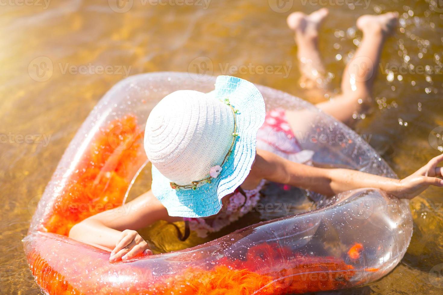 chica con sombrero nadando en el río con un círculo inflable transparente en forma de corazón con plumas naranjas dentro.el mar con un fondo arenoso. vacaciones en la playa, nadar, broncearse, protectores solares. foto