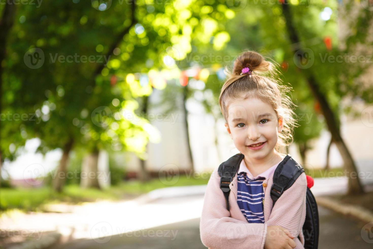 A little girl of Caucasian appearance in a school uniform with a backpack looks into the frame. Concept back to school. The first class, developing activities for preschoolers. Space for text photo