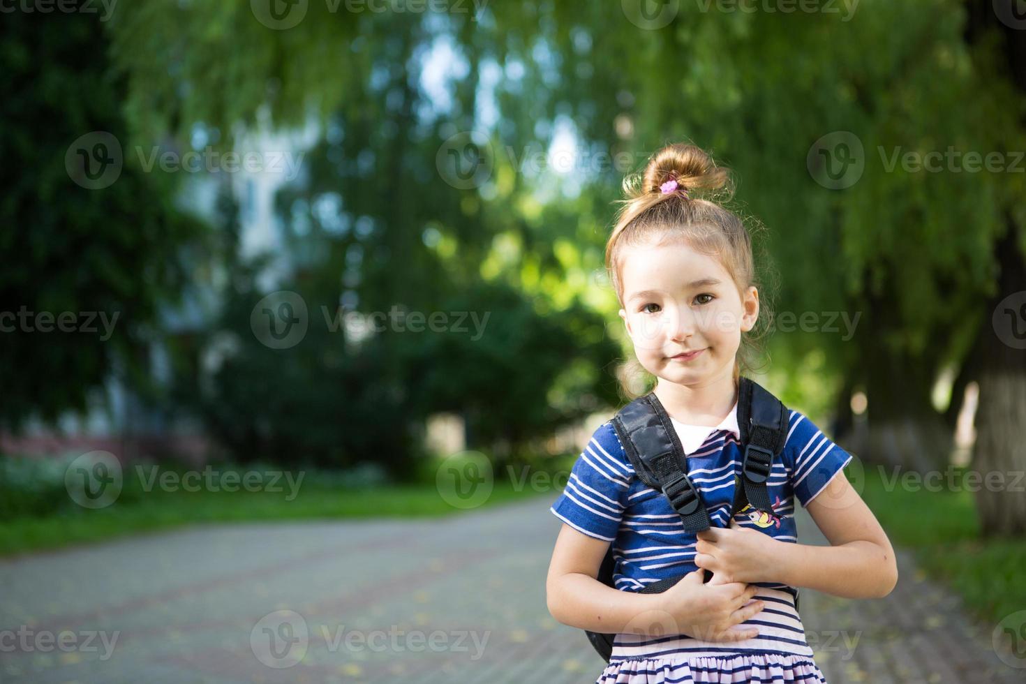 A little girl of Caucasian appearance in a school uniform with a backpack looks into the frame. Concept back to school. Elementary school, developing activities for preschoolers. Space for text photo