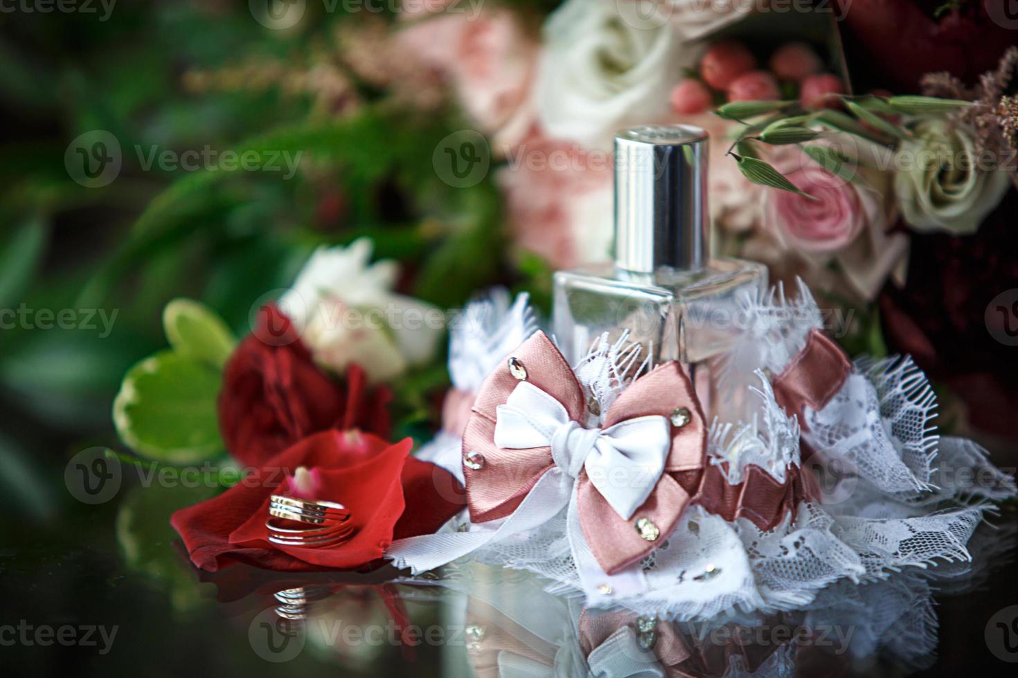 accesorios de boda para la novia y el novio un ramo de rosas rojas, rosadas y blancas, un boutonniere, anillos de boda de oro, una liga de encaje con un lazo, perfume. joyería, floristería. espacio para texto foto