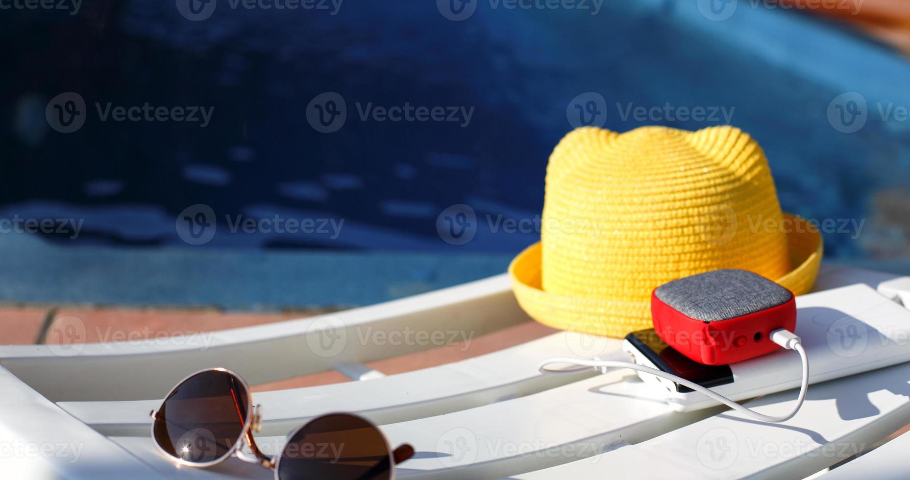 el altavoz portátil de música se carga desde el banco de energía a través de usb en una tumbona cerca de la piscina con accesorios de playa. siempre en contacto, dispositivos de viaje, batería externa para un teléfono inteligente. lugar para el texto. foto