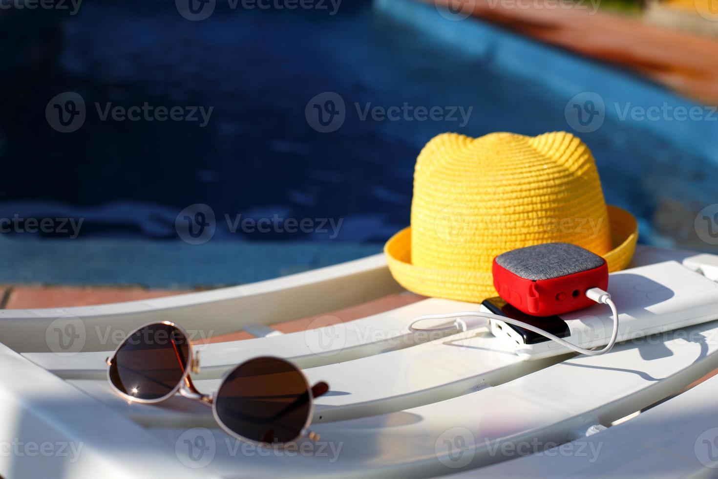 Music portable speaker is charged from the power bank via usb on a deck chair near the pool with beach accessories. Always in touch, travel gadgets, external battery for a smartphone. Place for text. photo