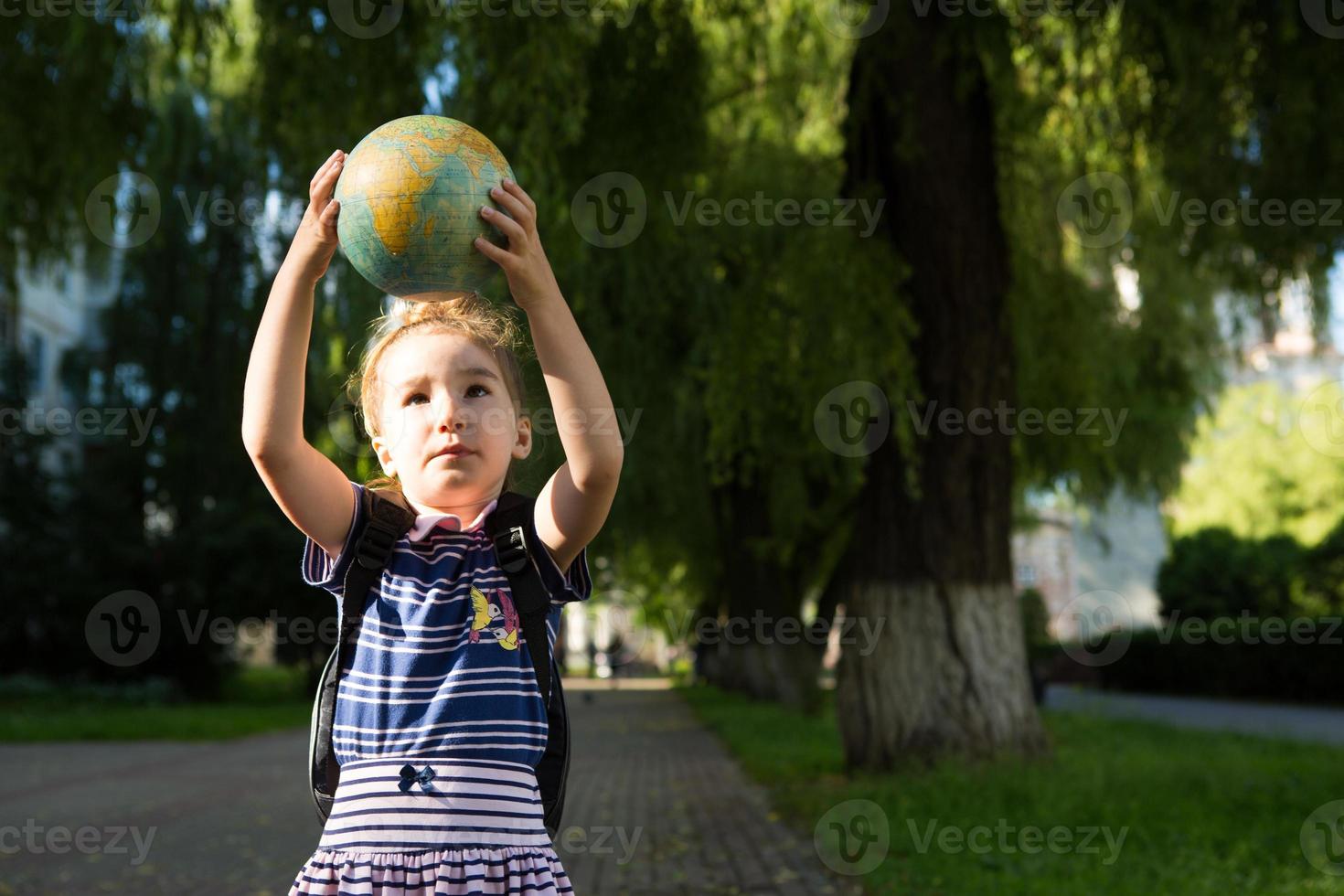 Kaluga, Russia-June 23, 2020. A girl from an elementary school of Caucasian appearance with a backpack on her shoulders holds a globe in her hands and carefully studies it. photo