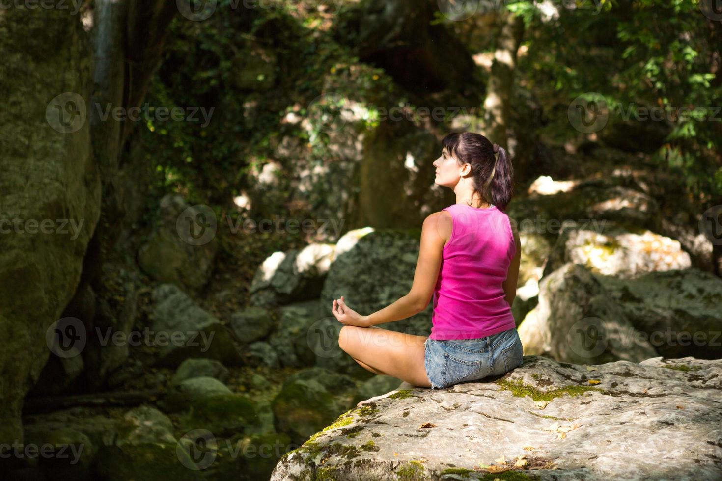 una mujer se sienta en un campo de loto sobre una gran roca entre las rocas al aire libre y medita, disfruta de la unidad con la naturaleza, escucha el silencio y los sonidos del bosque. ecología foto