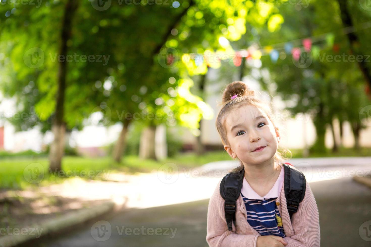 una niña de apariencia caucásica con uniforme escolar y mochila mira hacia el marco. concepto de regreso a la escuela. primaria, desarrollando actividades para preescolares. espacio para texto foto