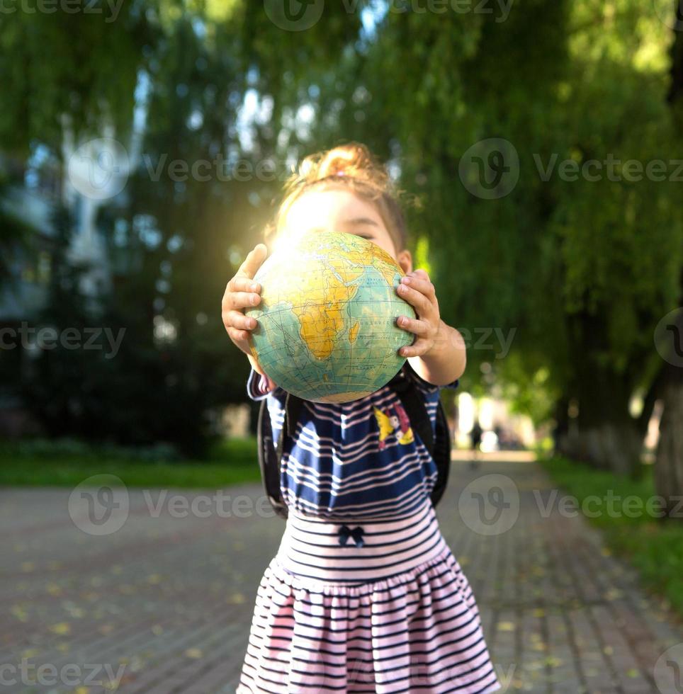 Kaluga, Russia-June 23, 2020. A girl from an elementary school of Caucasian appearance with a backpack on her shoulders holds a globe in her hands and carefully studies it. photo