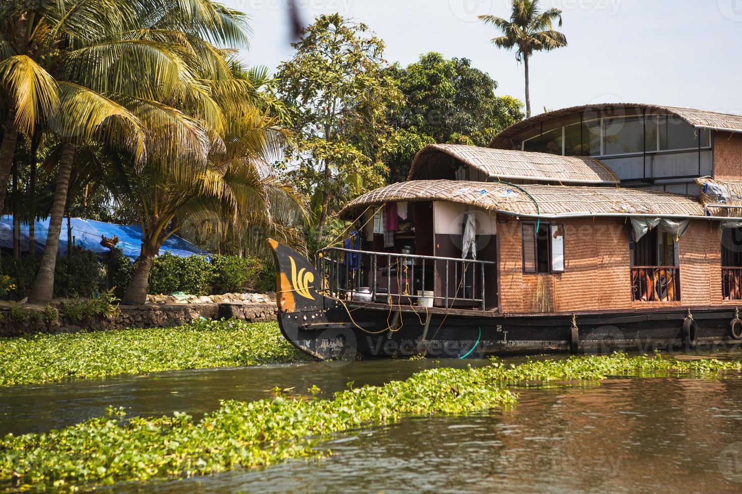 crucero de recreo de casa flotante en india, kerala en los canales fluviales cubiertos de algas de allapuzha en india. barco en el lago bajo el sol brillante y palmeras entre los trópicos. vista casa flotante foto