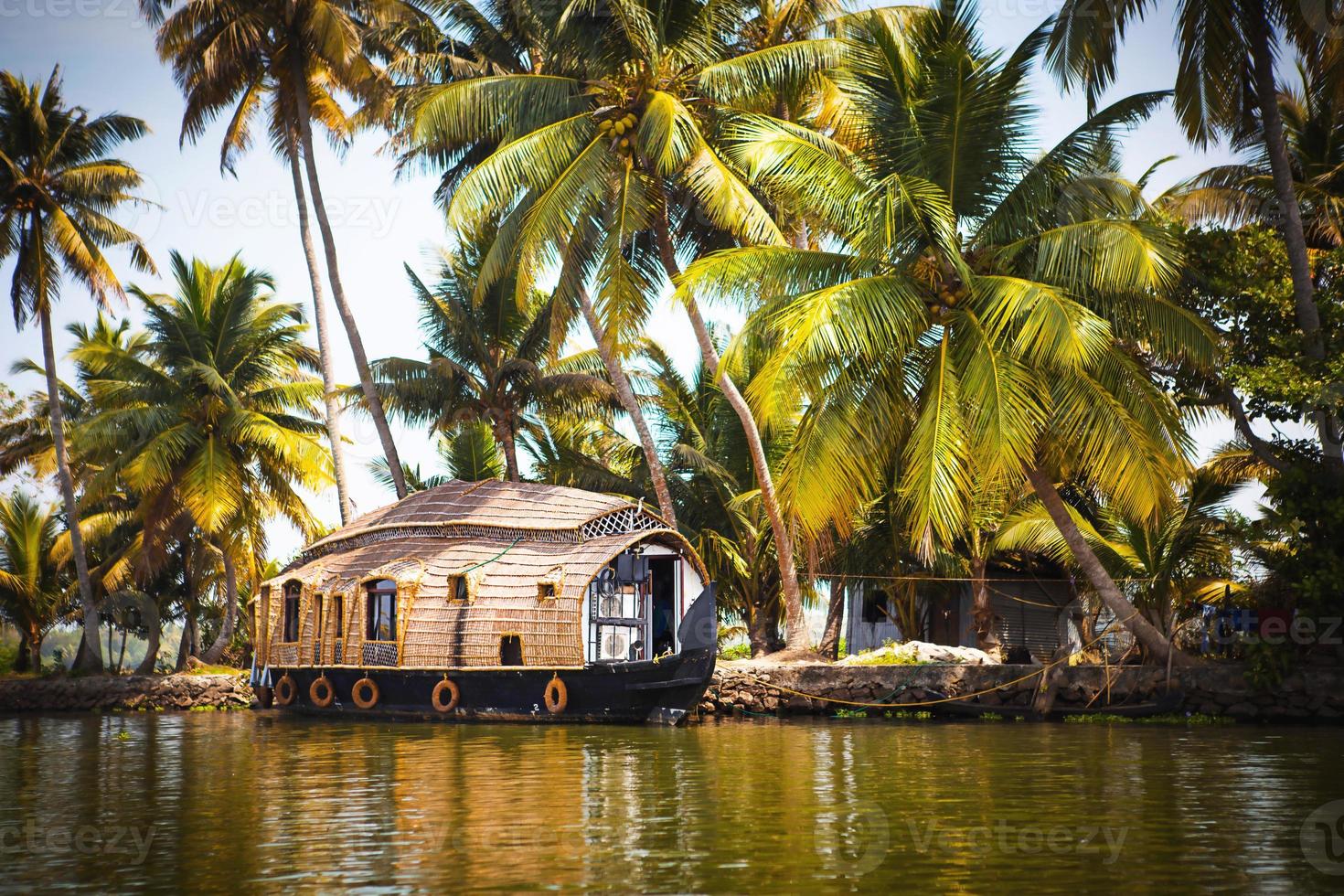 crucero de recreo de casa flotante en india, kerala en los canales fluviales cubiertos de algas de allapuzha en india. barco en el lago bajo el sol brillante y palmeras entre los trópicos. vista casa flotante foto