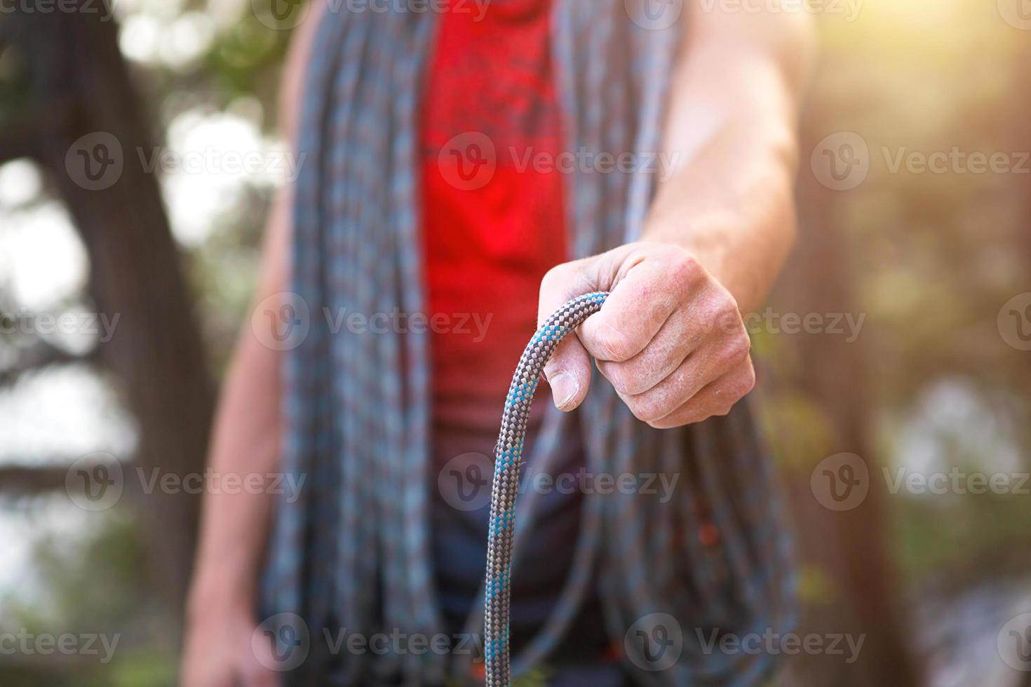 A male climber of Caucasian appearance with a coiled rope in his hand. Rope winding, knot, equipment storage. Hand in white magnesia. Red sports Jersey, extreme sports, rock climbing. Lifestyle photo