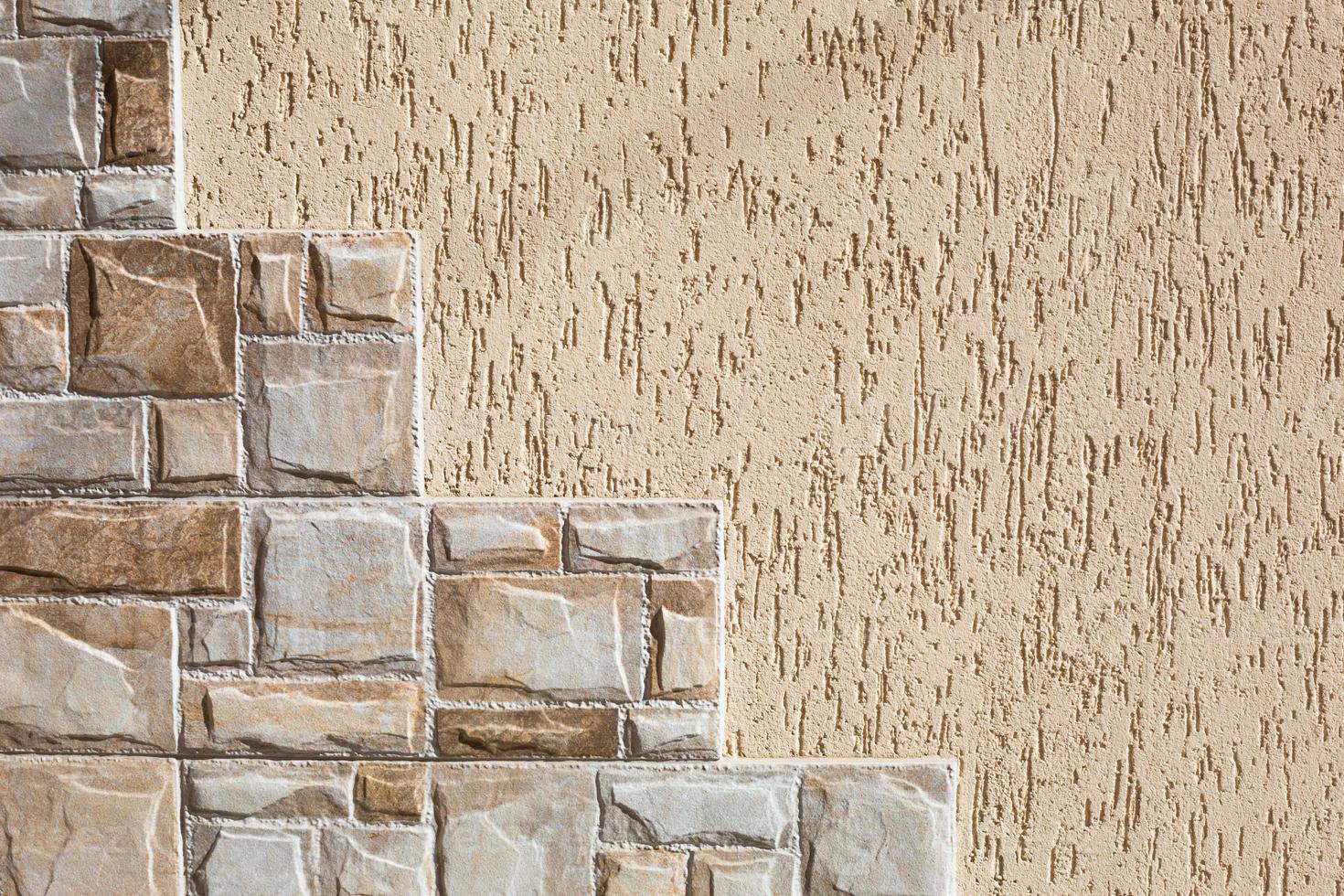 Stone tiles in the form of steps made of rectangular fragments of beige and sand color and plaster on the wall with a bark beetle pattern. Background, texture. Exterior decoration of building, house. photo