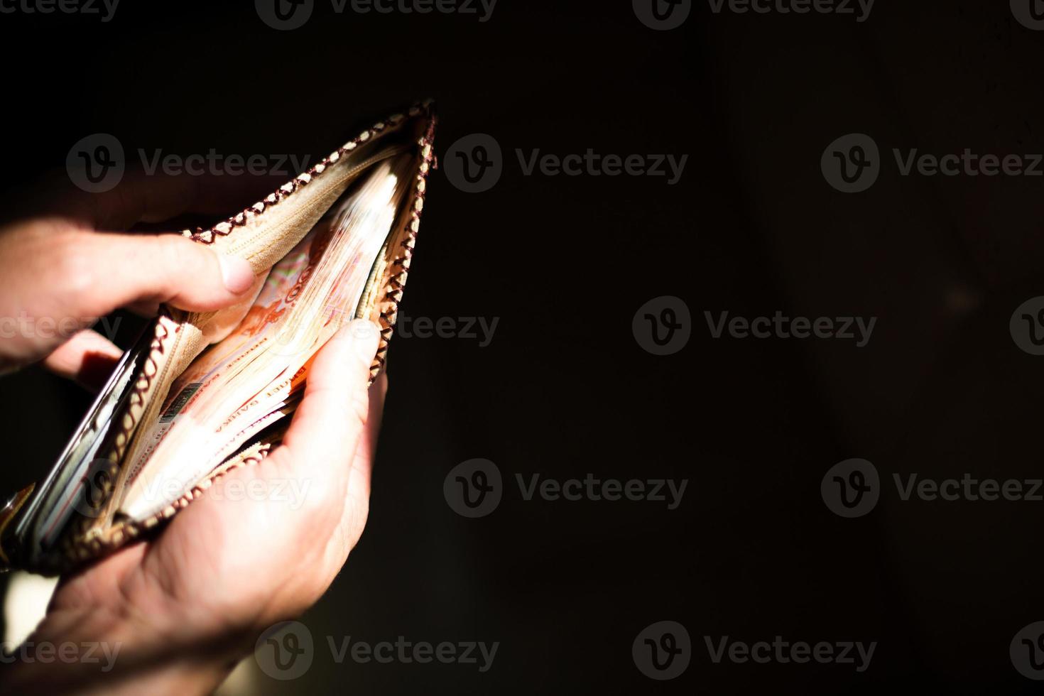 billetera de cuero llena de dinero ruso-5000 billetes, cinco mil rublos. la mano de un hombre sostiene una billetera abierta y desbordante contra un fondo negro en un haz de luz. copie el espacio foto