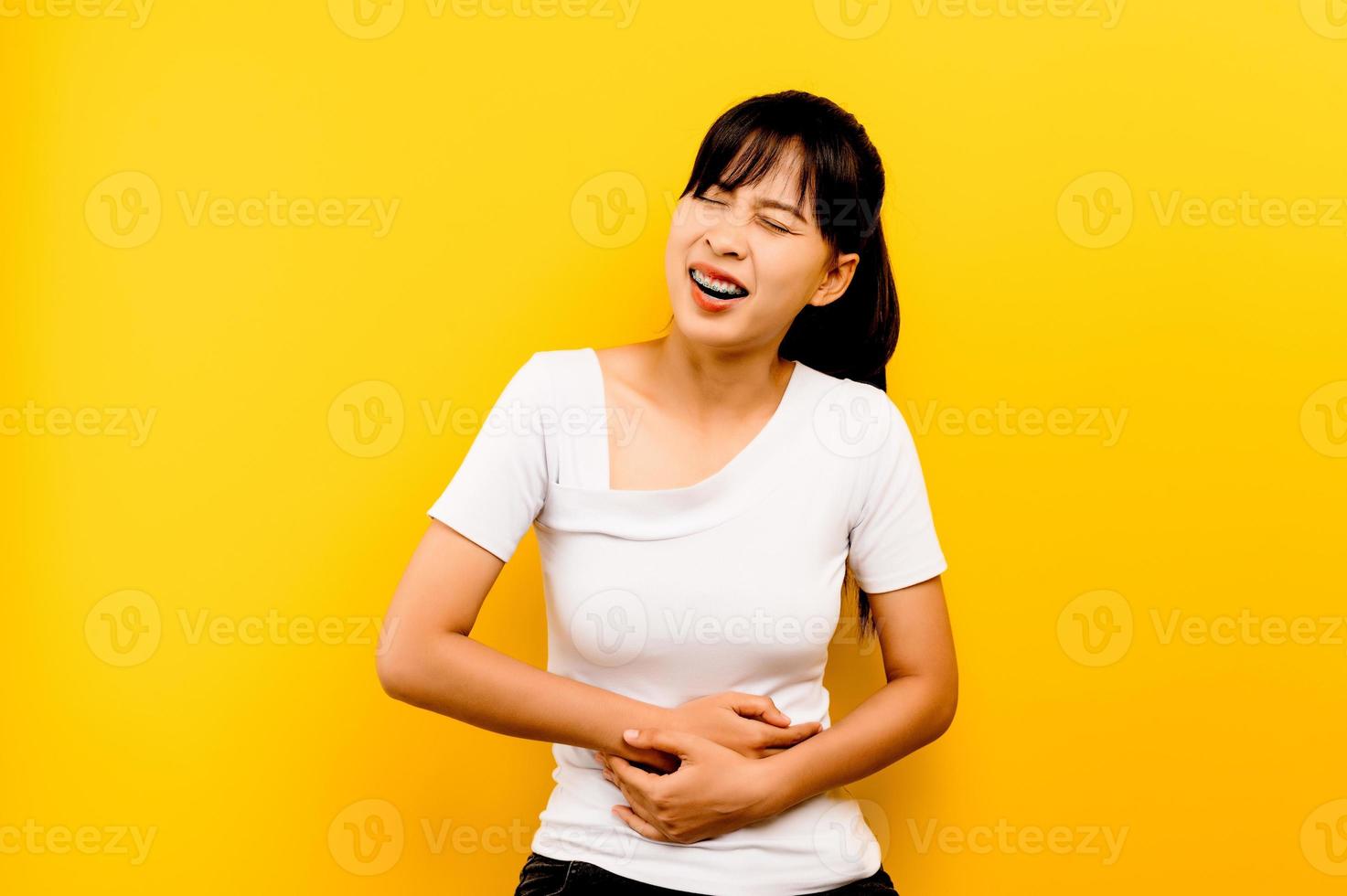 Severe abdominal pain woman hugging stomach isolated on yellow background photo