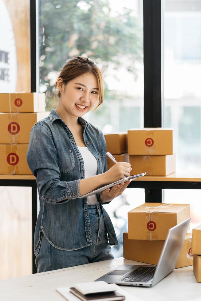 emprendedor de pequeñas empresas, autónomo, retrato de mujer joven que trabaja en la oficina en casa, caja, teléfono inteligente, computadora portátil, en línea, marketing, empaque, entrega, pyme, concepto de comercio electrónico foto