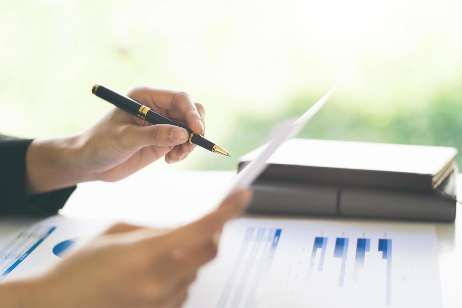 Close up of businesswoman holding a pen and pointing at the information sheet on his desk, reading the company's financials to make a financial plan. Financial concept. photo