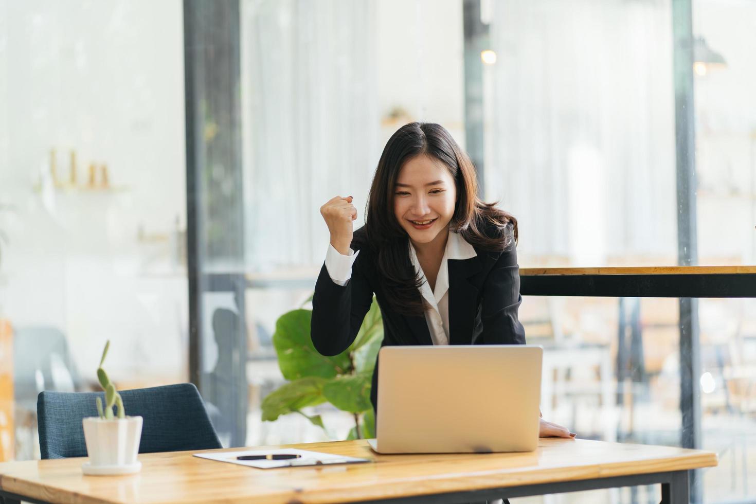 Excited young woman standing at table with laptop and celebrating success photo