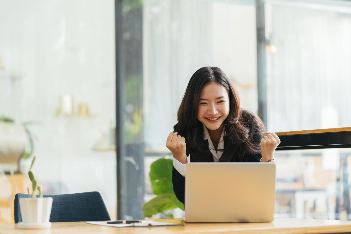 una mujer asiática emocionada sentada en el escritorio se siente eufórica al ganar la lotería en línea, una mujer negra feliz encantada de recibir un correo en una computadora portátil que se promociona en el trabajo, una chica birracial asombrada lee buenas noticias en la computadora foto