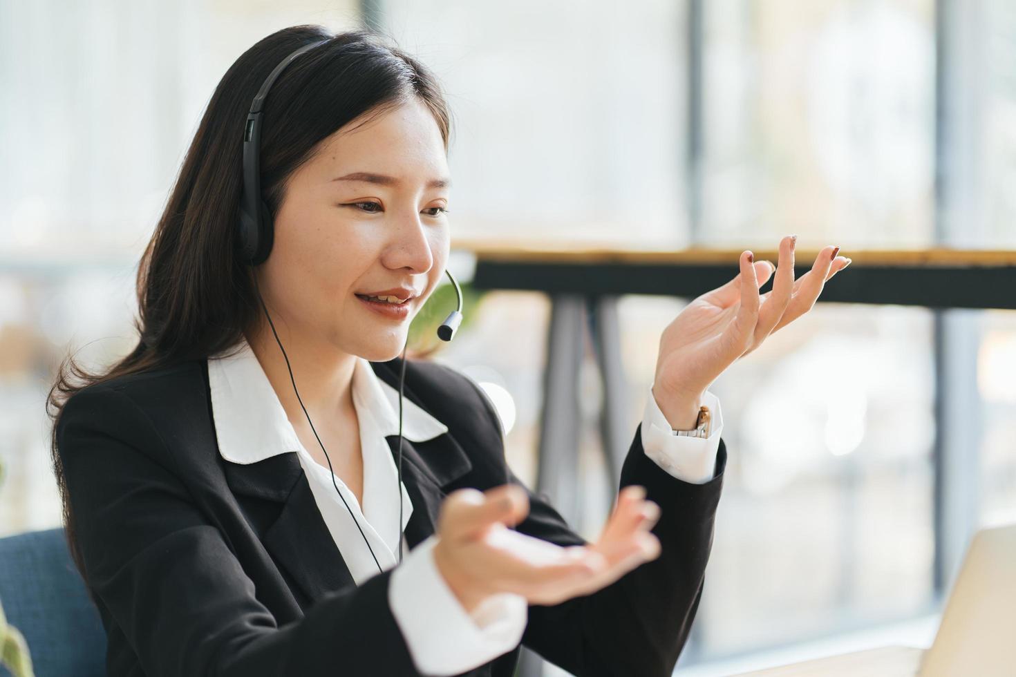 Side view head shot smiling asian lady freelancer wearing headset, communicating with client via video computer call. Millennial pleasant professional female tutor giving online language class. photo