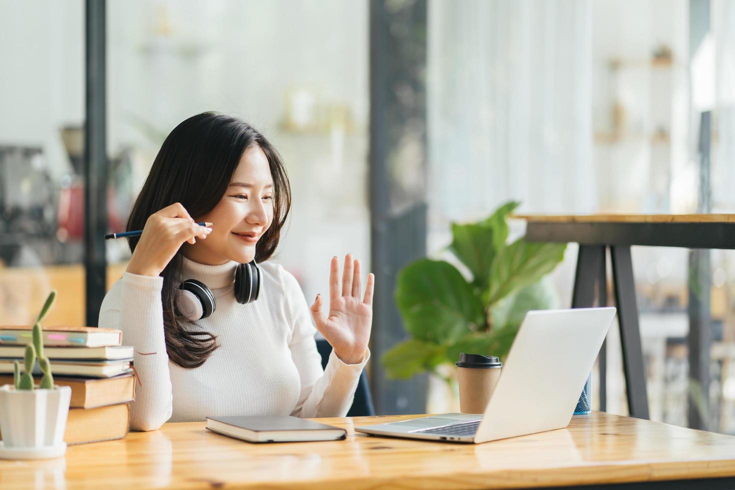 Happy young asian woman waving hand talking with remote web teacher on social distance video conference call elearning class on computer. Girl learning at home photo