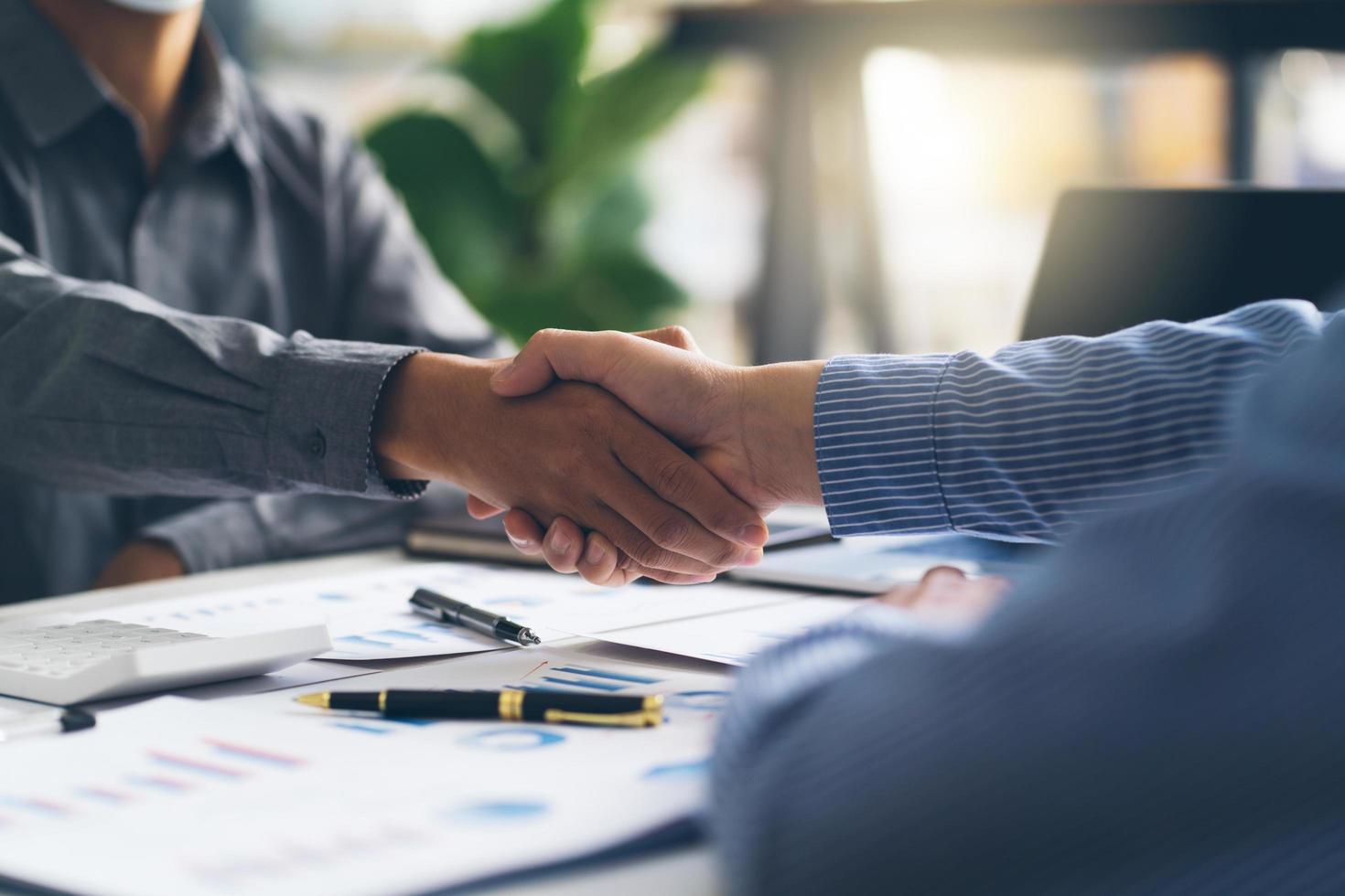 Entrepreneurs collaboration deal shaking hands in a modern office and financial paper graph on desk. photo