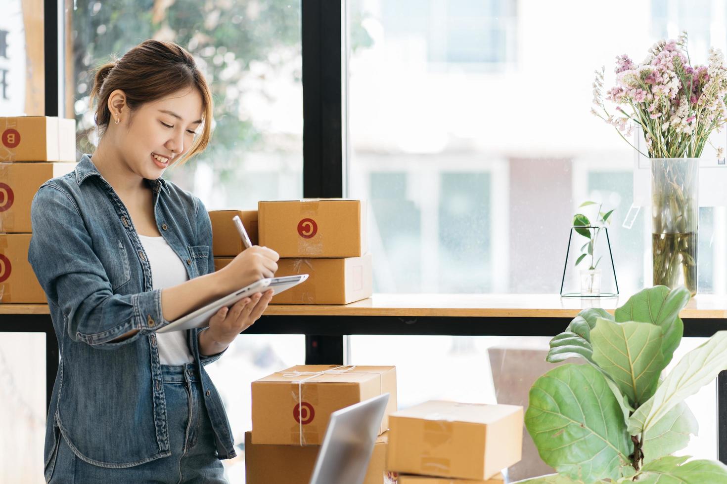 mujer empacando un artículo que vende en línea. joven propietario de una pequeña empresa empacando una caja de cartón en el lugar de trabajo. una vendedora independiente prepara una caja de paquetes de productos para entregar al cliente. foto